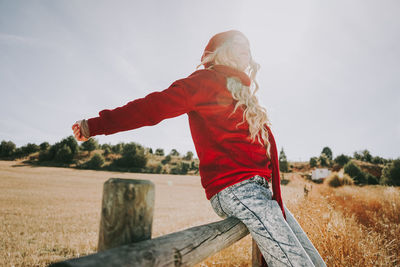 Woman sitting on railing in field against sky