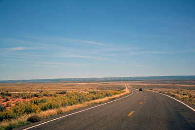 Road passing through landscape against clear blue sky