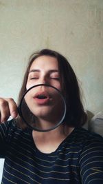 Close-up of young woman holding magnifying glass against wall