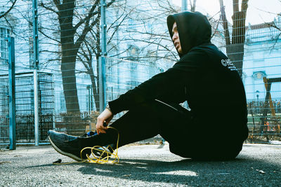 Side view of man sitting on sidewalk in city