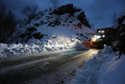 Snow covered road amidst field during winter at night