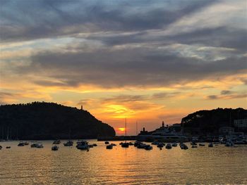 Silhouette buildings by sea against sky during sunset