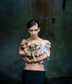 Portrait of shirtless woman holding puppies against wall