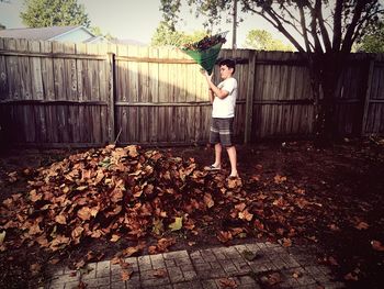 Boy with broom standing in yard against fence