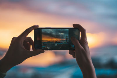 Low section of person photographing mobile phone against sunset sky