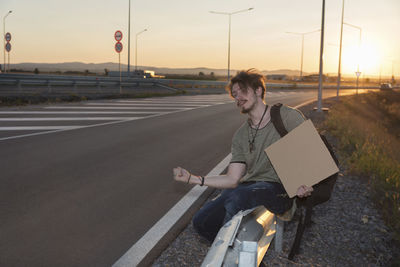 Side view of man gesturing while standing by road against sky