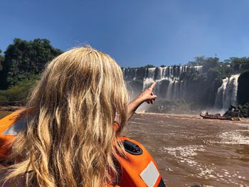 Rear view of woman pointing while rafting against waterfall and sky