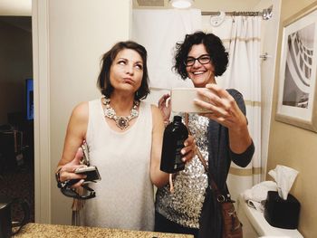 Portrait of young woman holding smart phone while standing on mirror