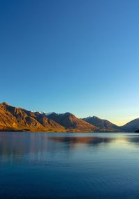 Scenic view of lake and mountains against clear blue sky