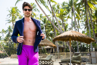 Full length of man wearing sunglasses standing against palm trees