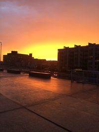 Silhouette buildings by river against sky during sunset