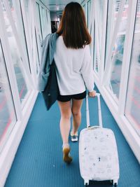 Rear view of woman with luggage walking in corridor