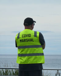 Rear view of man standing by sea against sky