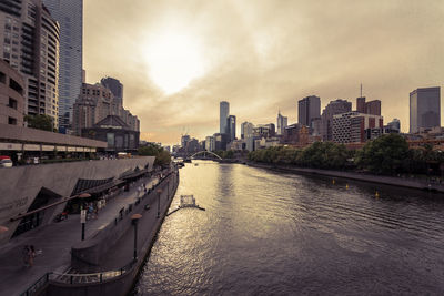 View of city at waterfront against cloudy sky