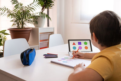 Rear view of man using laptop on table at home