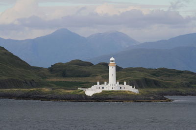 Lighthouse by sea against mountain range