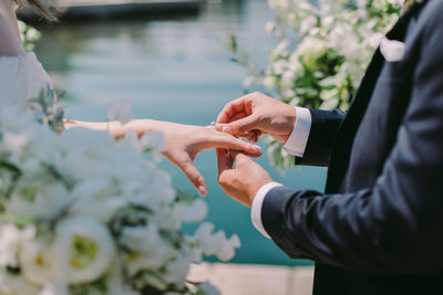 Midsection of groom putting ring on bride finger