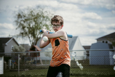 Teenage boy hitting ball while standing on playing field