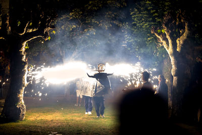 Rear view of people on field against sky at night