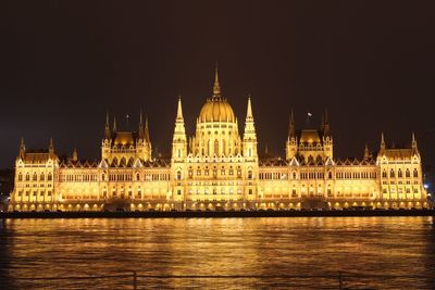 Illuminated hungarian parliament building by river against sky at night