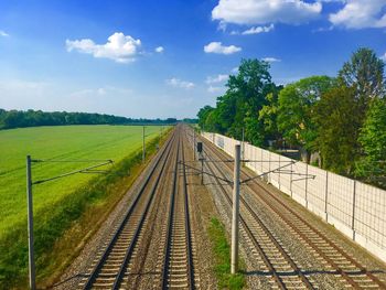 Railroad tracks amidst trees on field against sky