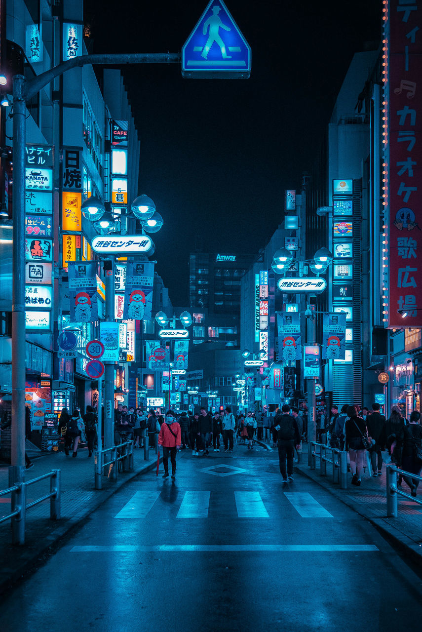 PEOPLE WALKING ON ILLUMINATED STREET AT NIGHT