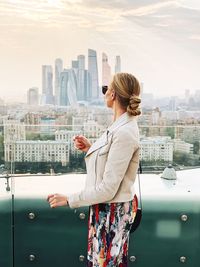 Woman standing by cityscape against sky in city