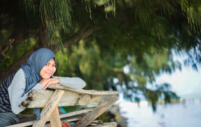 Portrait of smiling woman in hijab siting on bench at lakeshore