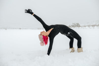 Side view of graceful female practicing yoga in kapotasana on snowy field in winter