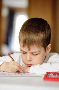 Cute and smiling cucasian boy draws with colored pencils while sitting at the table. 