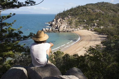 Rear view of woman sitting on rock by sea