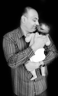 Happy father holding son against black background