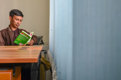 Young man reading book while sitting in office