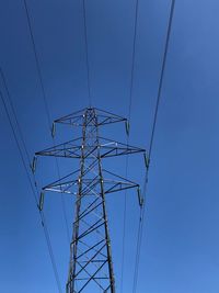 Low angle view of electricity pylon against clear blue sky