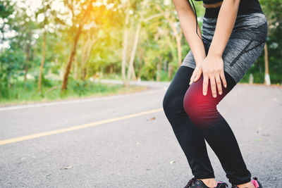 Midsection of woman wearing sports clothing with knee pain standing on road