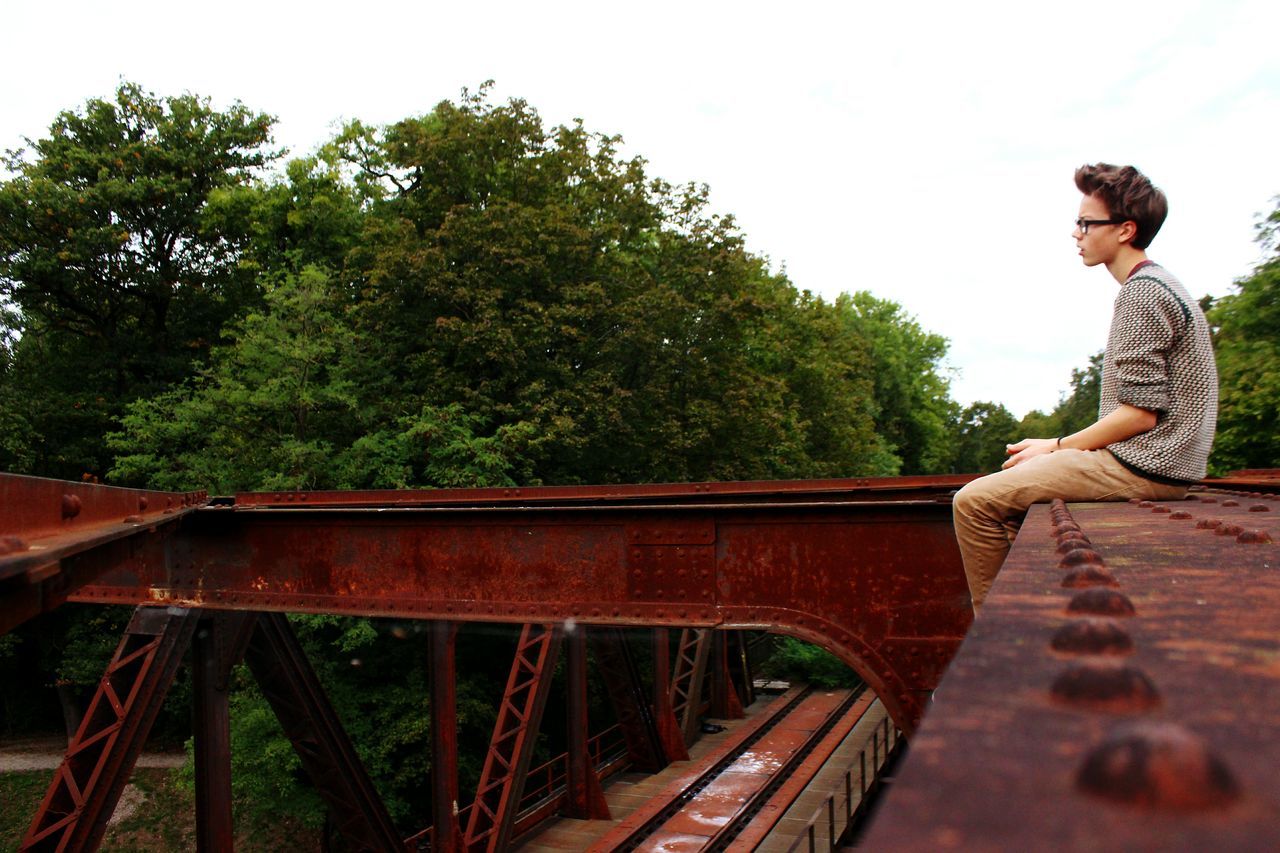 tree, lifestyles, leisure activity, railing, casual clothing, full length, built structure, standing, young adult, steps, low angle view, men, architecture, day, person, bridge - man made structure, young men, outdoors