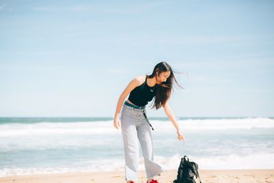 Young woman standing at beach against sky