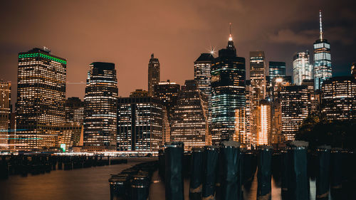 Illuminated buildings by river against sky at night