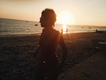 Woman standing at beach against sky during sunset