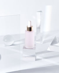 Glass bottle of pink hyaluronic acid for skin care treatment placed on table amidst glass geometric figures in light room