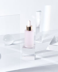 Glass bottle of pink hyaluronic acid for skin care treatment placed on table amidst glass geometric figures in light room