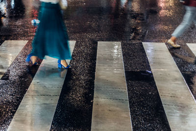 Low section of woman crossing wet zebra crossing at night