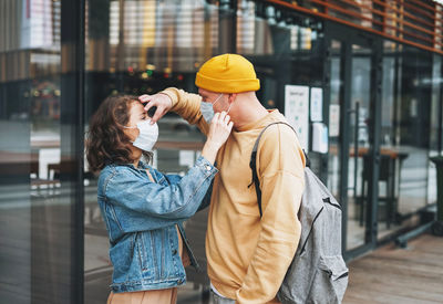 Stylish young family couple hipsters in face mask against glass building, new normal