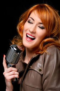 Young beautiful woman singing with vintage microphone against black background