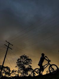 Low angle view of silhouette man riding bicycle against sky
