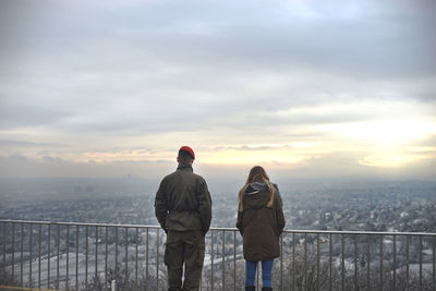 Rear view of man and woman standing by railing against sky