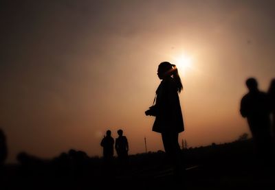 Silhouette friends standing against orange sky during sunset