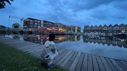 Rear view of woman standing by river against cloudy sky