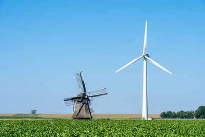 An old traditional windmill among a number of modern wind turbines under a clear blue sky