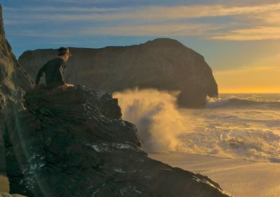 Man sitting on rock formation at beach during sunset